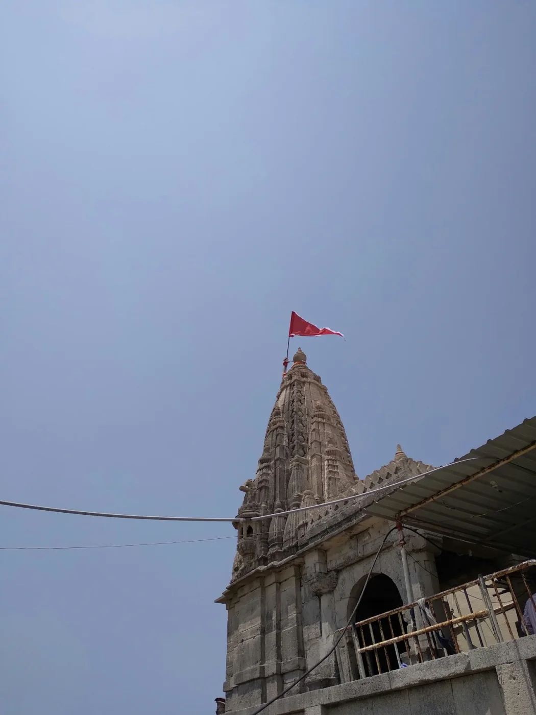 A temple shikhara with a flag against the sky in Gujarat