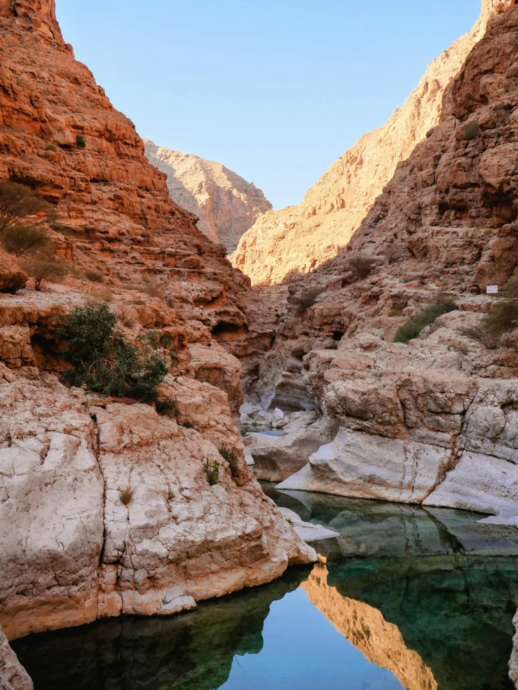 A sunlit canyon with a turquoise pool at Wadi Shab, Oman