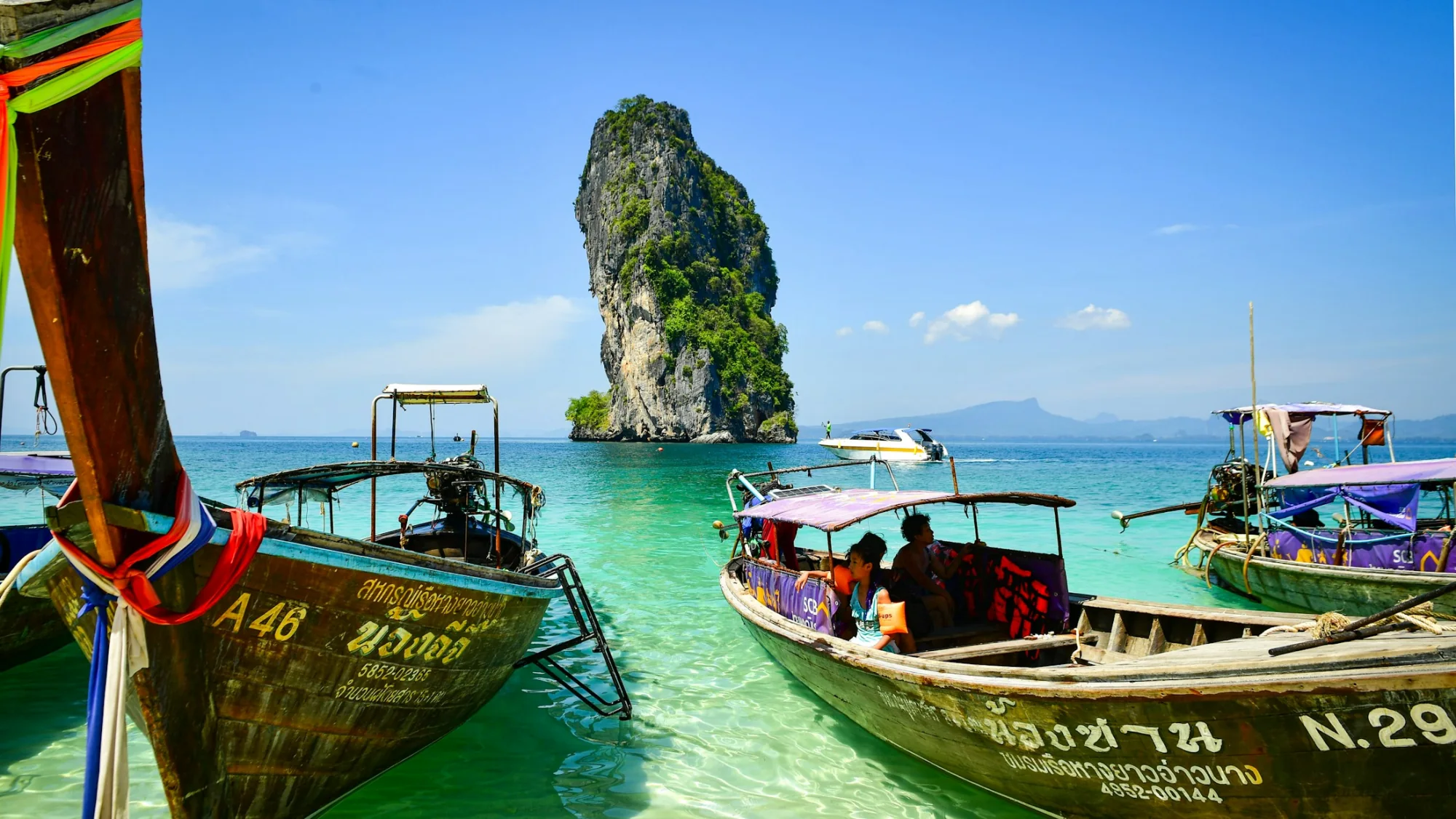 Longtail boats on clear turquoise water near a limestone island, Thailand